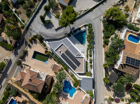 Aerial view of a modern villa with solar panels on the roof surrounded by swimming pools palm trees and residential streets in Moraira Valencian Community Spain.