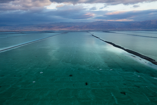 Aerial view of shimmering turquoise salt ponds stretching towards distant rugged mountains under a dramatic cloudy sky Sdom Israel. Aerial view of shimmering turquoise salt ponds stretching towards distant rugged mountains under a dramatic cloudy sky Sdom Israel.