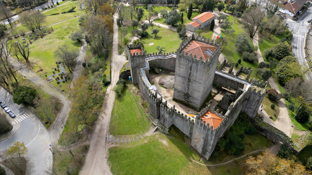 Aerial view of Guimaraes Castle featuring its medieval stone walls and crenelated towers surrounded by lush green parkland in Guimaraes Braga Portugal. Aerial view of Guimaraes Castle featuring its medieval stone walls and crenelated towers surrounded by lush green parkland in Guimaraes Braga Portugal.
