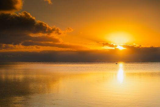 View of Aitutaki lagoon at sunset with golden light reflecting on the calm water and clouds in the sky Cook Islands. View of Aitutaki lagoon at sunset with golden light reflecting on the calm water and clouds in the sky Cook Islands.
