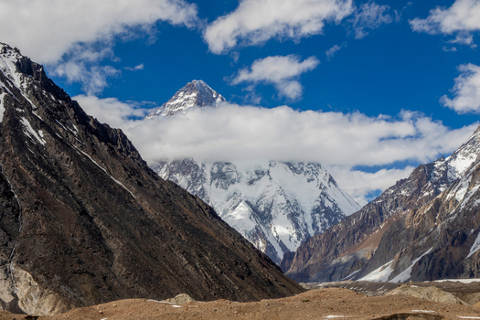 View of the snow capped peak of K2 mountain partially covered by white clouds under a blue sky in Skardu Gilgit Pakistan.