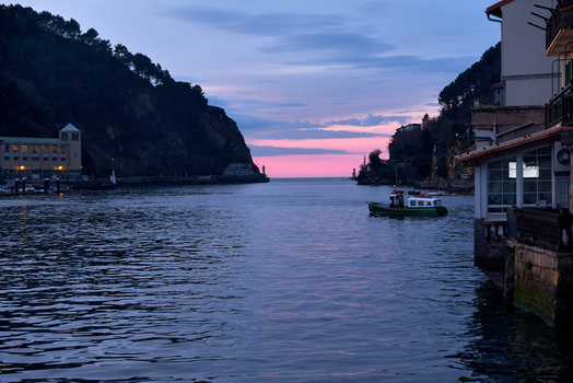 Pasai Donibane Spain 09 March 2026 View of the harbor street and a small boat on the water at twilight surrounded by steep hills and traditional coastal buildings.