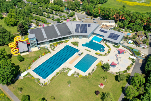 Aerial view of Konigsbad Forchheim featuring outdoor swimming pools with people water slides and sunbathing lawns surrounded by lush green trees in Forchheim Bayern Germany. Aerial view of Konigsbad Forchheim featuring outdoor swimming pools with people water slides and sunbathing lawns surrounded by lush green trees in Forchheim Bayern Germany.