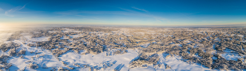 Aerial view of a vast snow covered landscape with dense forests and open fields under a clear blue sky in Latvia. Aerial view of a vast snow covered landscape with dense forests and open fields under a clear blue sky in Latvia.