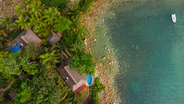 Axim Ghana 09 February 2023 Aerial view of Lou Moon Resort Eco Luxury featuring thatched roof villas with private pools nestled among lush palm trees along a rocky coastline and clear water. Axim Ghana 09 February 2023 Aerial view of Lou Moon Resort Eco Luxury featuring thatched roof villas with private pools nestled among lush palm trees along a rocky coastline and clear water.