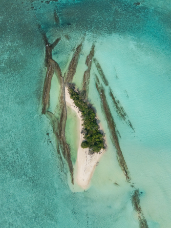 Aerial view of verdant island with white sands flanked by dark reefs in clear turquoise waters Thuraakunu Thiladhunmathee Uthuruburi Maldives. Aerial view of verdant island with white sands flanked by dark reefs in clear turquoise waters Thuraakunu Thiladhunmathee Uthuruburi Maldives.