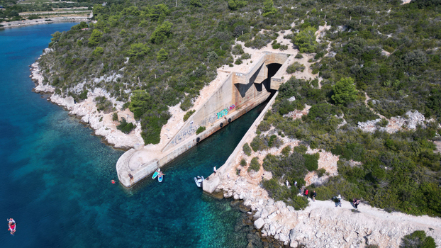 Aerial view of the Yugoslav army underground boat shelter Potkop Parja carved into the rocky coastline with turquoise water and lush greenery in Rogacic Splitsko dalmatinska Croatia. Aerial view of the Yugoslav army underground boat shelter Potkop Parja carved into the rocky coastline with turquoise water and lush greenery in Rogacic Splitsko dalmatinska Croatia.