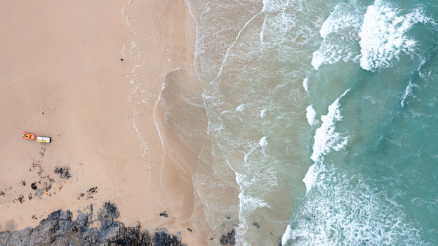 Aerial view of Constantine Bay with turquoise waves crashing on the sandy shore and a small boat on the beach in Padstow Cornwall United Kingdom. Aerial view of Constantine Bay with turquoise waves crashing on the sandy shore and a small boat on the beach in Padstow Cornwall United Kingdom.