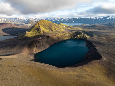 Aerial view of the volcanic crater lake Ljotipollur surrounded by vibrant green mossy mountains and snow capped peaks in the rugged landscape of Rangarthing ytra Iceland. Aerial view of the volcanic crater lake Ljotipollur surrounded by vibrant green mossy mountains and snow capped peaks in the rugged landscape of Rangarthing ytra Iceland.