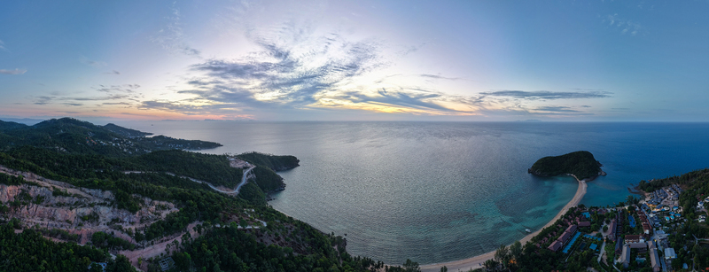 Aerial view of the coastline of Ko Pha Ngan with lush green hills a sandy beach turquoise waters and a scenic sunset sky in Ko Pha ngan District Surat Thani Thailand.