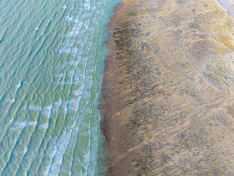 Aerial view of Beach of the Bois de Cise with turquoise waves washing over the textured rocky shoreline and sandy beach Ault Hauts de France France.