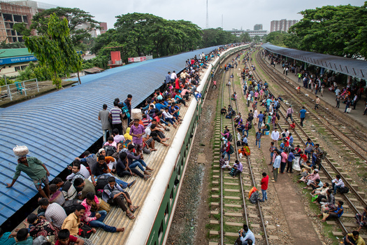 Dhaka Bangladesh 14 June 2018 View of Airport Railway Station with people sitting on the roof of a train and on the tracks surrounded by lush green trees. Dhaka Bangladesh 14 June 2018 View of Airport Railway Station with people sitting on the roof of a train and on the tracks surrounded by lush green trees.