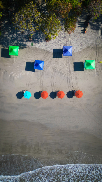 Aerial view of colorful beach umbrellas casting shadows on the sandy shore where the forest meets the ocean Quepos Puntarenas Province Costa Rica. Aerial view of colorful beach umbrellas casting shadows on the sandy shore where the forest meets the ocean Quepos Puntarenas Province Costa Rica.