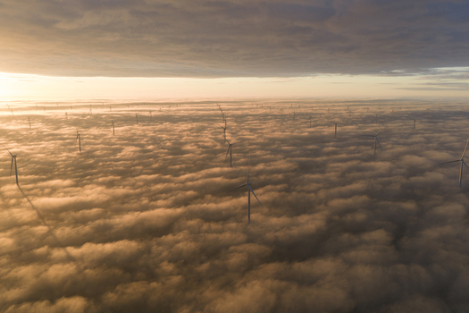 Aerial view of Windpark Fryslan wind turbines emerging from a dense layer of golden clouds during sunrise in Breezanddijk Friesland Netherlands.