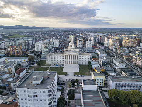 Fier Albania 18 January 2026 Aerial view of the University of Fier building surrounded by urban residential blocks paved squares and trees under a cloudy sky.