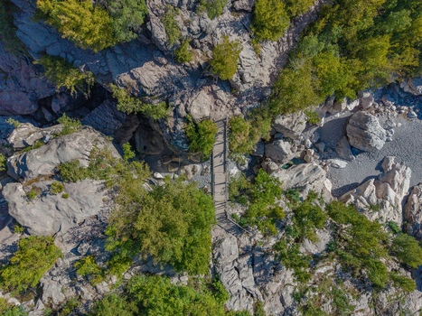 Aerial view of Blue Eye Theth featuring a wooden footbridge over rocky terrain surrounded by lush green trees and rugged cliffs Theth Shkoder County Albania. Aerial view of Blue Eye Theth featuring a wooden footbridge over rocky terrain surrounded by lush green trees and rugged cliffs Theth Shkoder County Albania.