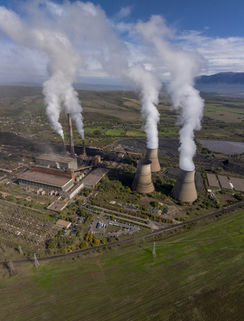 Aerial view of a thermal power plant with large cooling towers emitting steam into the sky surrounded by rolling hills and rural landscape in Bulgaria.