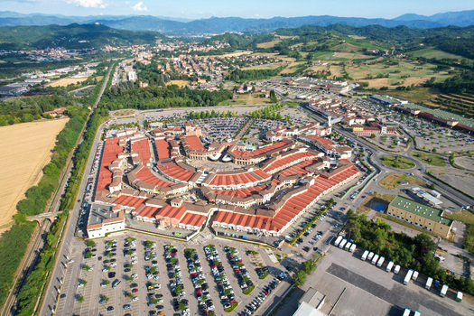 Aerial view of Designer Outlet Serravalle with its distinctive red roofed buildings and large parking areas surrounded by the rolling hills of Serravalle Scrivia Piemonte Italy. Aerial view of Designer Outlet Serravalle with its distinctive red roofed buildings and large parking areas surrounded by the rolling hills of Serravalle Scrivia Piemonte Italy.