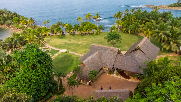 Axim Ghana 09 February 2023 Aerial view of Lou Moon Resort Eco Luxury featuring thatched roof buildings nestled among lush palm trees and green lawns along the coastline. Axim Ghana 09 February 2023 Aerial view of Lou Moon Resort Eco Luxury featuring thatched roof buildings nestled among lush palm trees and green lawns along the coastline.