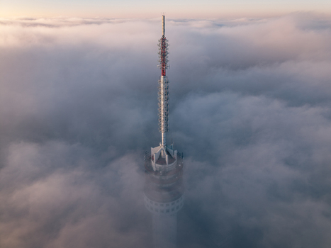 Aerial view of a tall telecommunications tower piercing through a thick layer of clouds under a soft morning light in Roermond Limburg Netherlands.