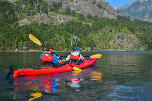 View of two people paddling a red tandem kayak on the calm waters of Nahuel Huapi Lake with lush green forests and mountains San Carlos de Bariloche Rio Negro Argentina. View of two people paddling a red tandem kayak on the calm waters of Nahuel Huapi Lake with lush green forests and mountains San Carlos de Bariloche Rio Negro Argentina.