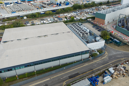 Aerial view of a modern data center building with large rooftop cooling units situated in an industrial area with surrounding roads and infrastructure in the United Kingdom. Aerial view of a modern data center building with large rooftop cooling units situated in an industrial area with surrounding roads and infrastructure in the United Kingdom.