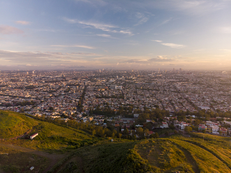 Aerial view of the sprawling urban landscape at sunset featuring dense residential buildings distant city skyline and grassy hills in the foreground in Tlaquepaque Jalisco Mexico. Aerial view of the sprawling urban landscape at sunset featuring dense residential buildings distant city skyline and grassy hills in the foreground in Tlaquepaque Jalisco Mexico.