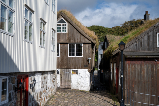 View of traditional wooden houses with grass turf roofs and stone foundations along a cobblestone path in the historic Tinganes district Faroe Islands. View of traditional wooden houses with grass turf roofs and stone foundations along a cobblestone path in the historic Tinganes district Faroe Islands.