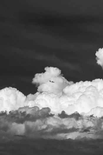 View of a small airplane flying against a backdrop of large dramatic cumulus clouds in the sky over Costa Rica.