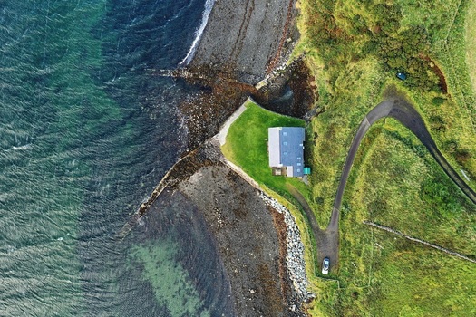 Aerial view of a solitary house situated on a grassy cliff edge overlooking the rocky coastline and deep blue sea in Stein Scotland United Kingdom. Aerial view of a solitary house situated on a grassy cliff edge overlooking the rocky coastline and deep blue sea in Stein Scotland United Kingdom.
