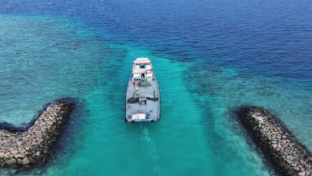 Aerial view of a boat navigating a channel between breakwaters Maldives. Aerial view of a boat navigating a channel between breakwaters Maldives.