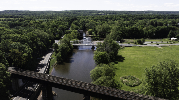 Aerial view of Neshanic Station featuring a historic railroad bridge spanning the river surrounded by lush green trees and open fields in Branchburg New Jersey United States. Aerial view of Neshanic Station featuring a historic railroad bridge spanning the river surrounded by lush green trees and open fields in Branchburg New Jersey United States.
