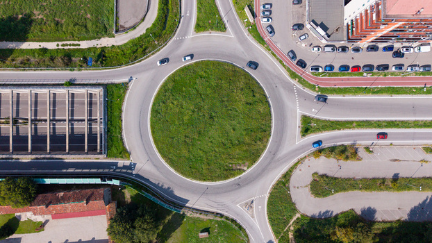 Aerial view of a roundabout with cars circulating on the asphalt a central green island and surrounding urban infrastructure in Milan Lombardy Italy.