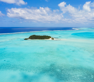 Aerial view of Aitutaki One Foot Island surrounded by vibrant turquoise lagoon waters and a coral reef under a bright blue sky in Arutanga Cook Islands. Aerial view of Aitutaki One Foot Island surrounded by vibrant turquoise lagoon waters and a coral reef under a bright blue sky in Arutanga Cook Islands.