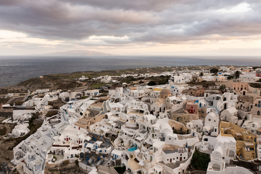 Aerial view of white buildings cascading down the cliffs towards the sea under a brooding sky Oia Thira Greece. Aerial view of white buildings cascading down the cliffs towards the sea under a brooding sky Oia Thira Greece.