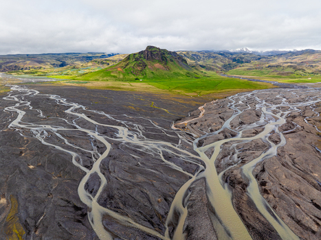 Aerial view of a braided river system with dark volcanic sand channels and glacial water flowing through a green landscape in Iceland. Aerial view of a braided river system with dark volcanic sand channels and glacial water flowing through a green landscape in Iceland.