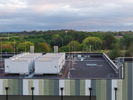Aerial view of a data center rooftop featuring industrial HVAC cooling units set against a backdrop of lush green trees and a cloudy sky in the United Kingdom. Aerial view of a data center rooftop featuring industrial HVAC cooling units set against a backdrop of lush green trees and a cloudy sky in the United Kingdom.