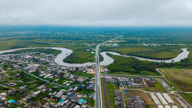 Aerial view of the winding Kwa Ibo River flowing through lush green mangroves and residential areas with a long bridge crossing the water in Kwa Ibo Akwa Ibom Nigeria.