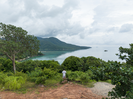 Aerial view of a person standing atop a reddish brown hill overlooking the lush green foliage and turquoise sea of Karimunjawa Island Karimunjawa Central Java Indonesia.