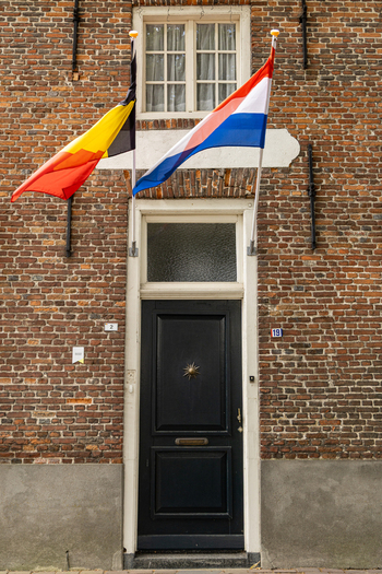 View of a black front door flanked by the national flags of Belgium and the Netherlands on a historic brick building facade in Baarle Nassau North Brabant Netherlands.