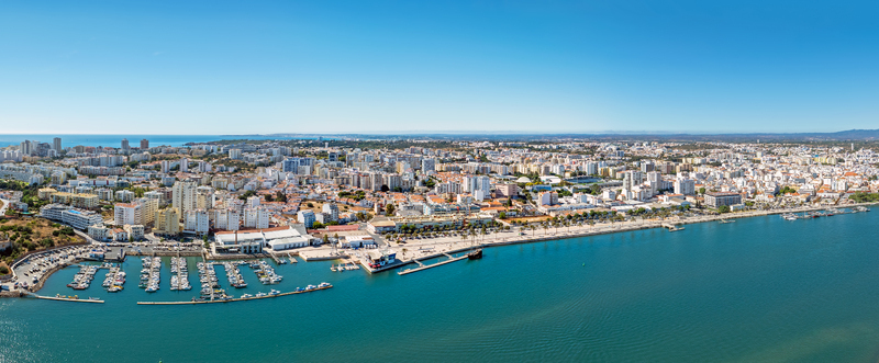 Aerial view of the marina and waterfront of Portimao with dense urban buildings palm trees along the promenade and the Atlantic coastline in Portimao Faro District Portugal. Aerial view of the marina and waterfront of Portimao with dense urban buildings palm trees along the promenade and the Atlantic coastline in Portimao Faro District Portugal.