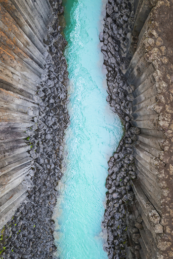 Aerial view of the basalt columns of Studlagil Canyon and the turquoise glacial river flowing through the gorge in Eiriksstadhir Mulathing Iceland. Aerial view of the basalt columns of Studlagil Canyon and the turquoise glacial river flowing through the gorge in Eiriksstadhir Mulathing Iceland.