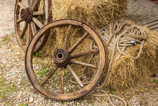 View of two vintage wooden wagon wheels leaning against hay bales with coiled rope on a gravel surface in Taujenai Vilnius County Lithuania.