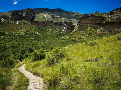 View of a hiking trail winding through the grassy slopes towards the dramatic sandstone cliffs of Golden Gate Highlands National Park in Clarens Free State South Africa. View of a hiking trail winding through the grassy slopes towards the dramatic sandstone cliffs of Golden Gate Highlands National Park in Clarens Free State South Africa.