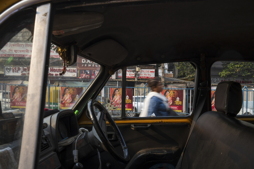 View of a woman walking past vibrant posters framed by the weathered interior of a classic yellow taxi in Kolkata West Bengal India. View of a woman walking past vibrant posters framed by the weathered interior of a classic yellow taxi in Kolkata West Bengal India.