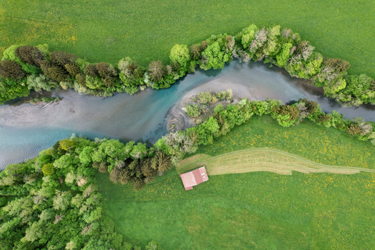 Aerial view of the winding river near Lac du Vernex flowing through lush green meadows and dense forests with a small wooden barn in Rossiniere Vaud Switzerland.