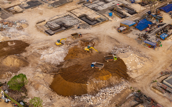 Aerial view of a resort development site with excavators and dump trucks working on the construction of building foundations in Kecamatan Kuta Selatan Bali Indonesia. Aerial view of a resort development site with excavators and dump trucks working on the construction of building foundations in Kecamatan Kuta Selatan Bali Indonesia.