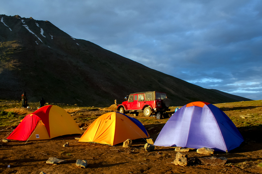View of colorful camping tents set up near a red off road vehicle with a dramatic mountain backdrop at Sheosar Lake in Skardu Pakistan. View of colorful camping tents set up near a red off road vehicle with a dramatic mountain backdrop at Sheosar Lake in Skardu Pakistan.