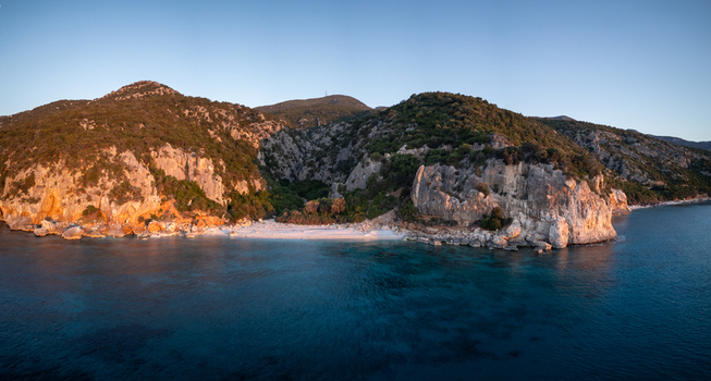 Aerial view of Spiaggia di Cala Fuili beach nestled between rugged limestone cliffs and lush vegetation by the turquoise sea in Dorgali Sardegna Italy. Aerial view of Spiaggia di Cala Fuili beach nestled between rugged limestone cliffs and lush vegetation by the turquoise sea in Dorgali Sardegna Italy.