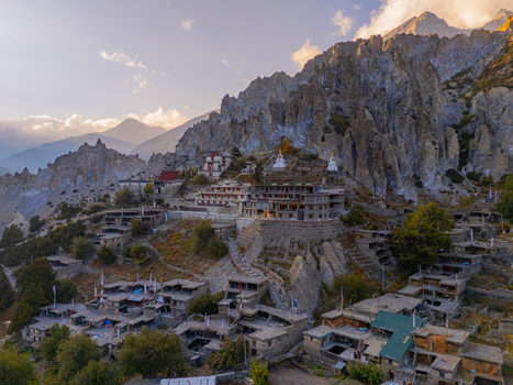 Aerial view of a traditional Himalayan village with stone houses and a monastery perched on a rocky cliffside under a clear sky in Nepal.